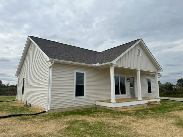 Two-story home with gray siding, white trim, covered front porch, large windows, and manicured grass lawn under a cloudy blue sky