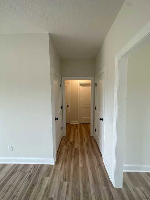 Hallway with white plaster walls, white doors featuring black knobs, warm wood laminate flooring, and ceiling light illuminating the space