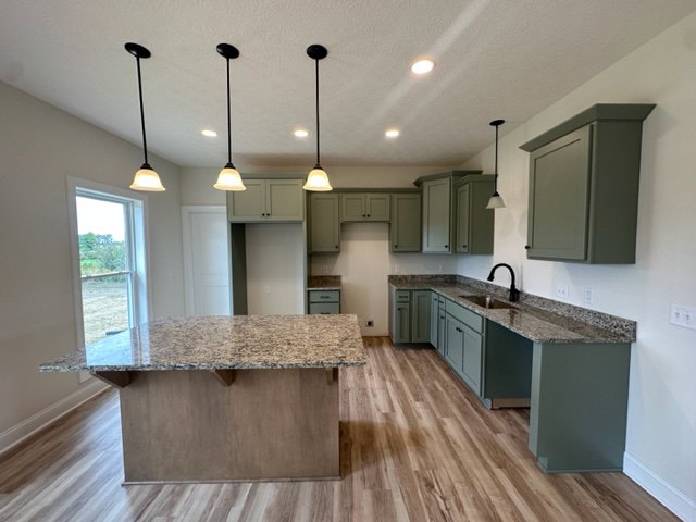 Spacious kitchen featuring a large central island with stone countertop, wood flooring, white cabinetry, stainless steel sink, and modern appliances