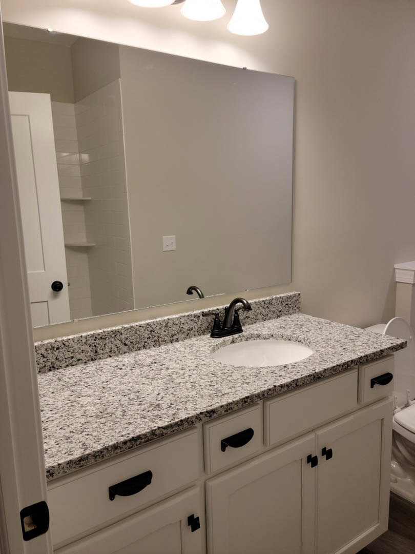 White quartz countertop with black specks, chrome faucet, undermount sink, flat-panel drawers, large frameless mirror, light gray tile backsplash