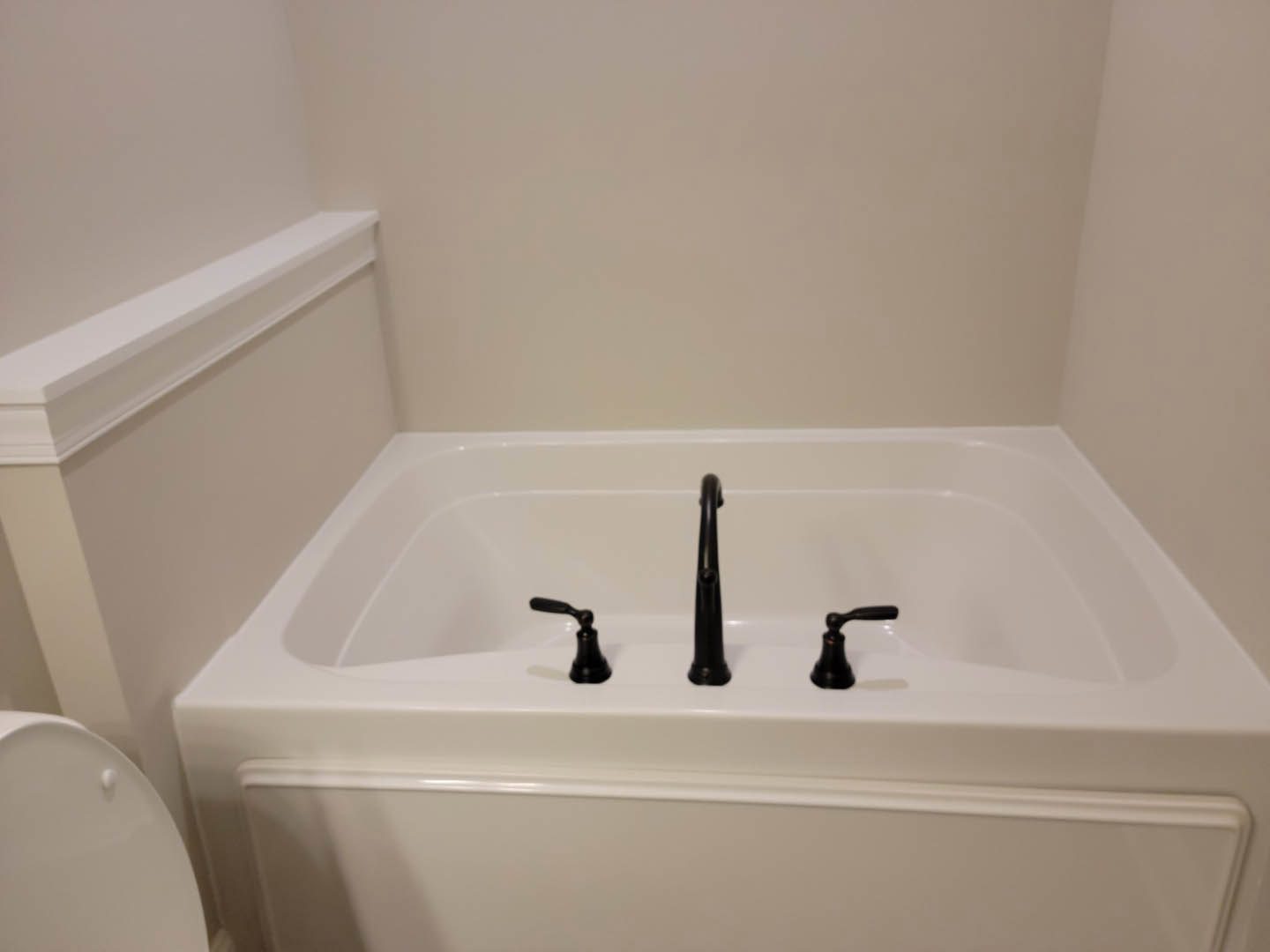White freestanding bathtub with matte black faucets beside a white toilet, set against a light-colored bathroom wall