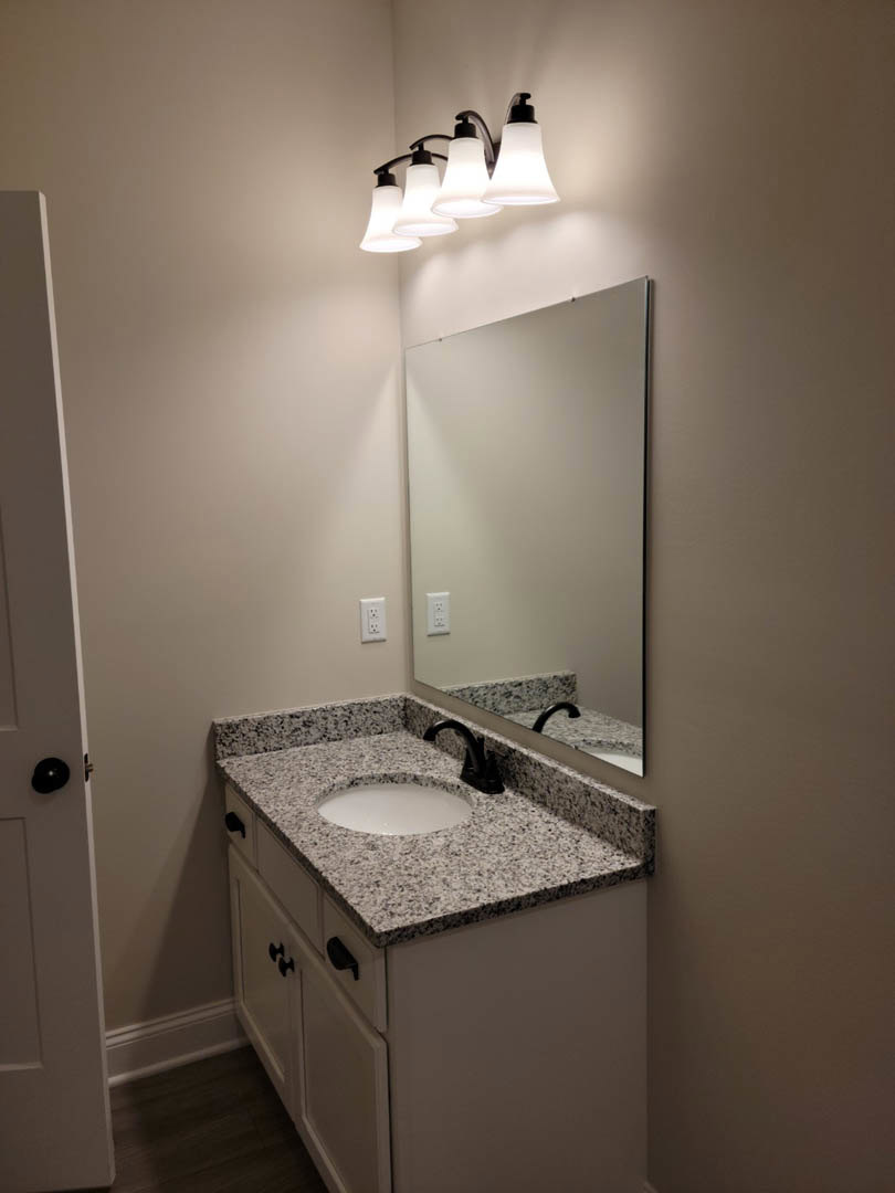 Modern bathroom with white tile walls, rectangular mirror above a sleek sink, chrome faucet, light fixture, and minimalist cabinetry with drawers