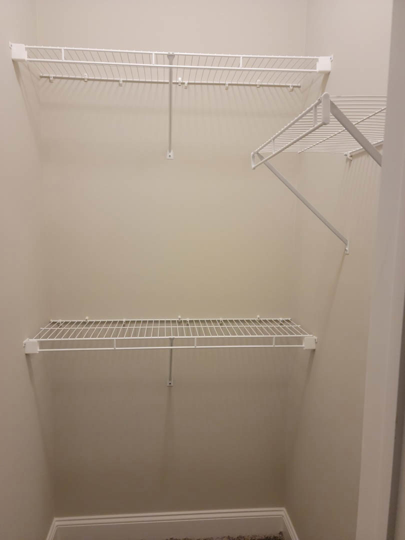 White closet with built-in shelves, white metal rack with hooks, and white door against smooth white walls.