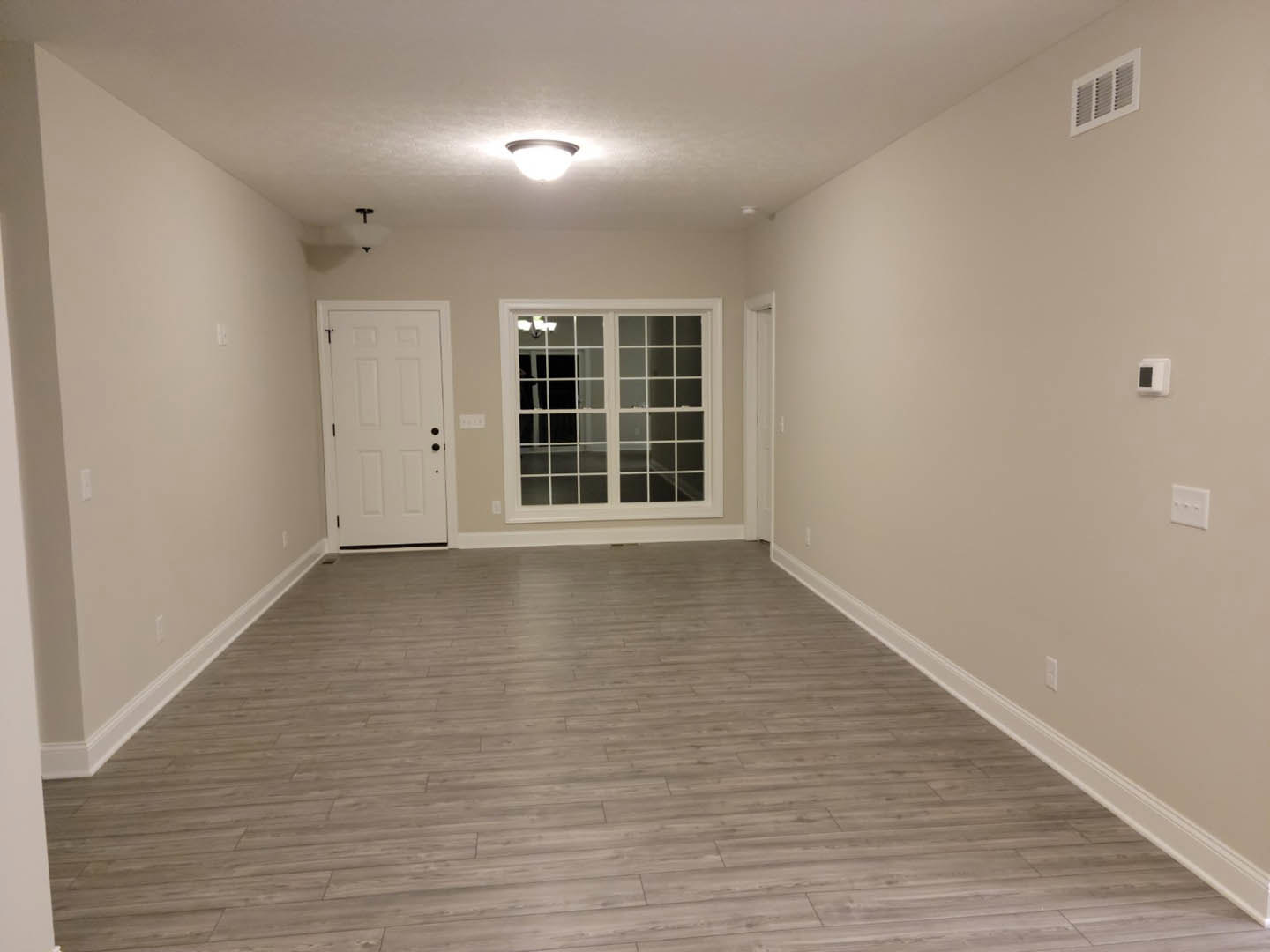 Room with wide-plank wood flooring, multi-pane window, white door with black hardware, plaster walls, and ceiling light fixture