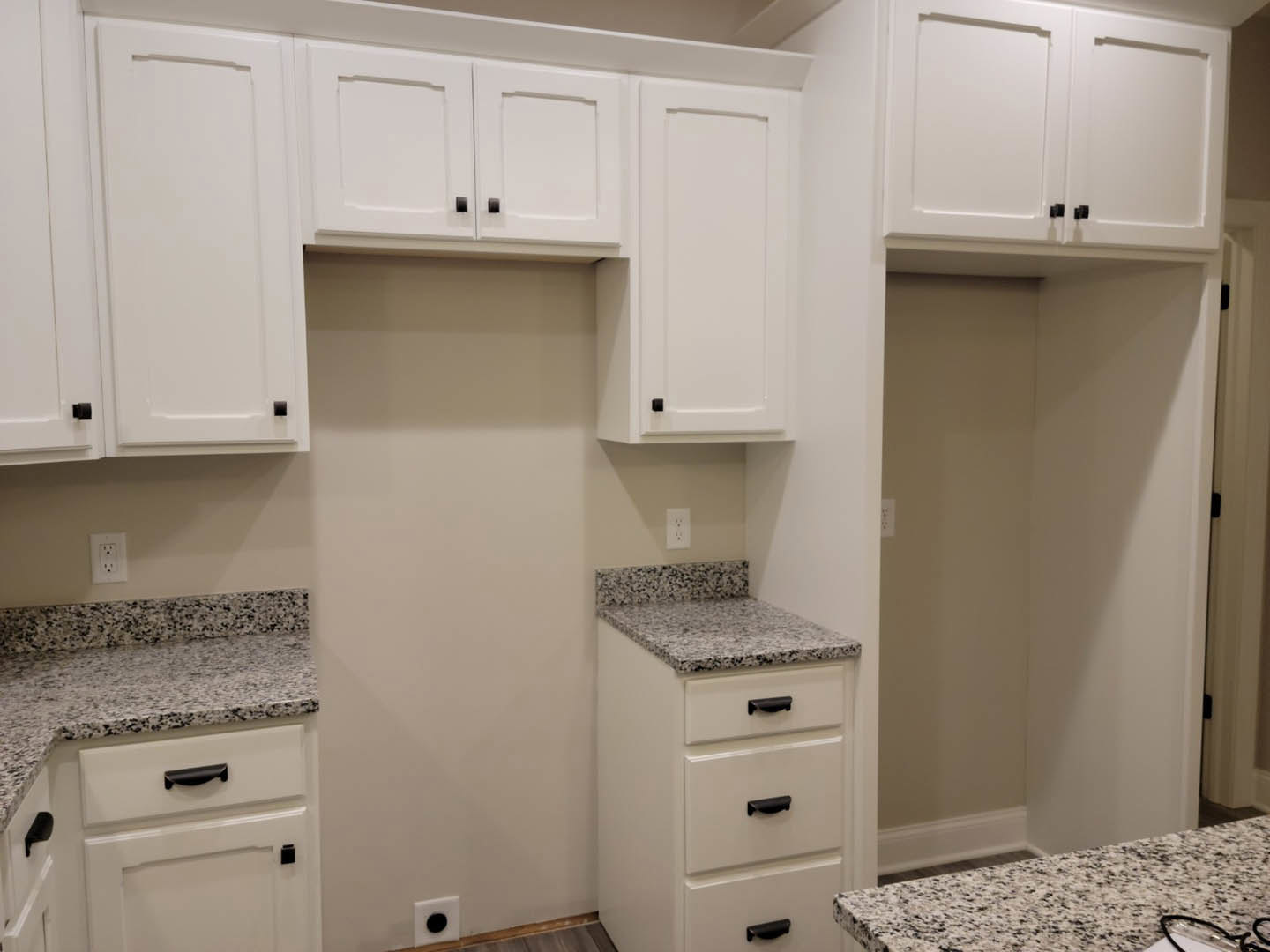 White kitchen cabinets and drawers, polished granite countertops, stainless steel sink, white electrical outlet, white interior door