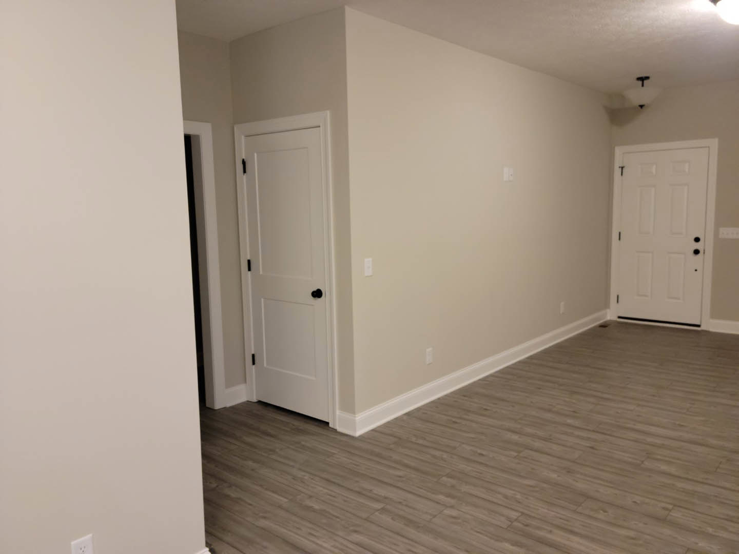 Hallway with white walls, wood laminate flooring, two white doors featuring black knobs
