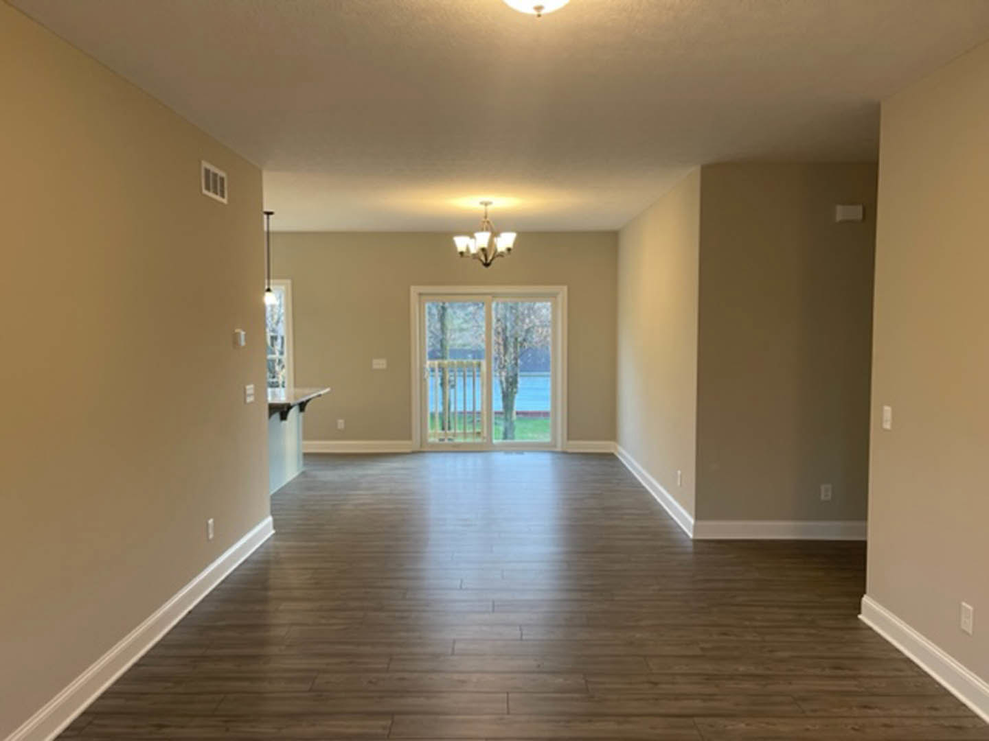 Open room with light wood flooring, white walls, single door, large window with metal railing overlooking trees, five-light ceiling fixture, glass door, and wall-mounted light