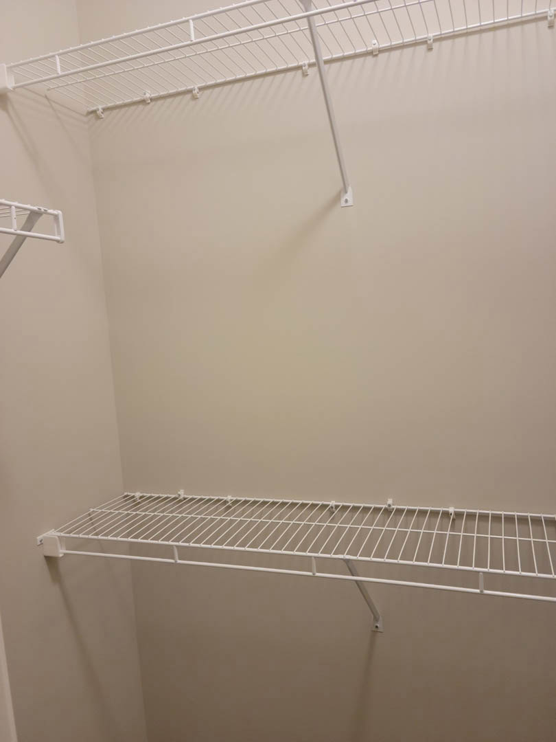 White wire shelf mounted on a white wall in a room, with a metal bar visible in close-up.