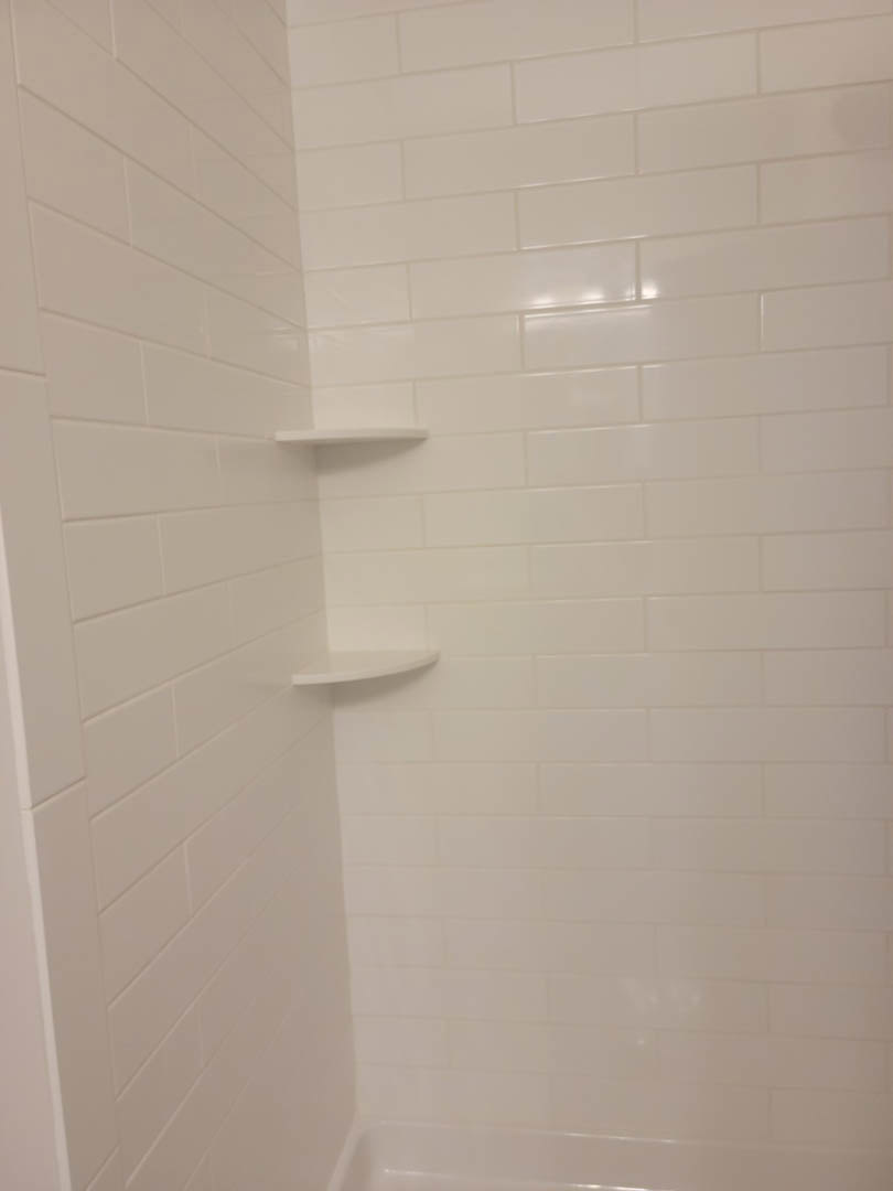 White tile shower with built-in shelves, chrome fixtures, and clean grout lines