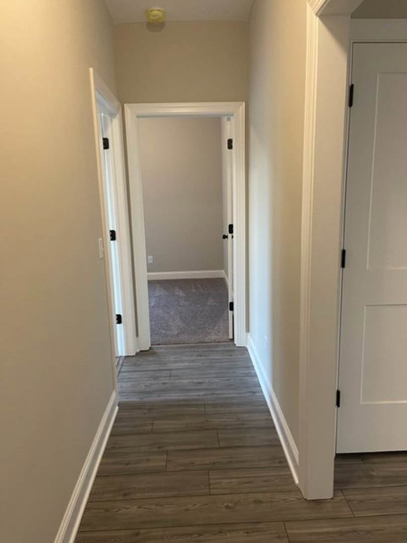 Hallway with smooth white walls, light wood laminate flooring, white baseboard trim, and a closed interior door