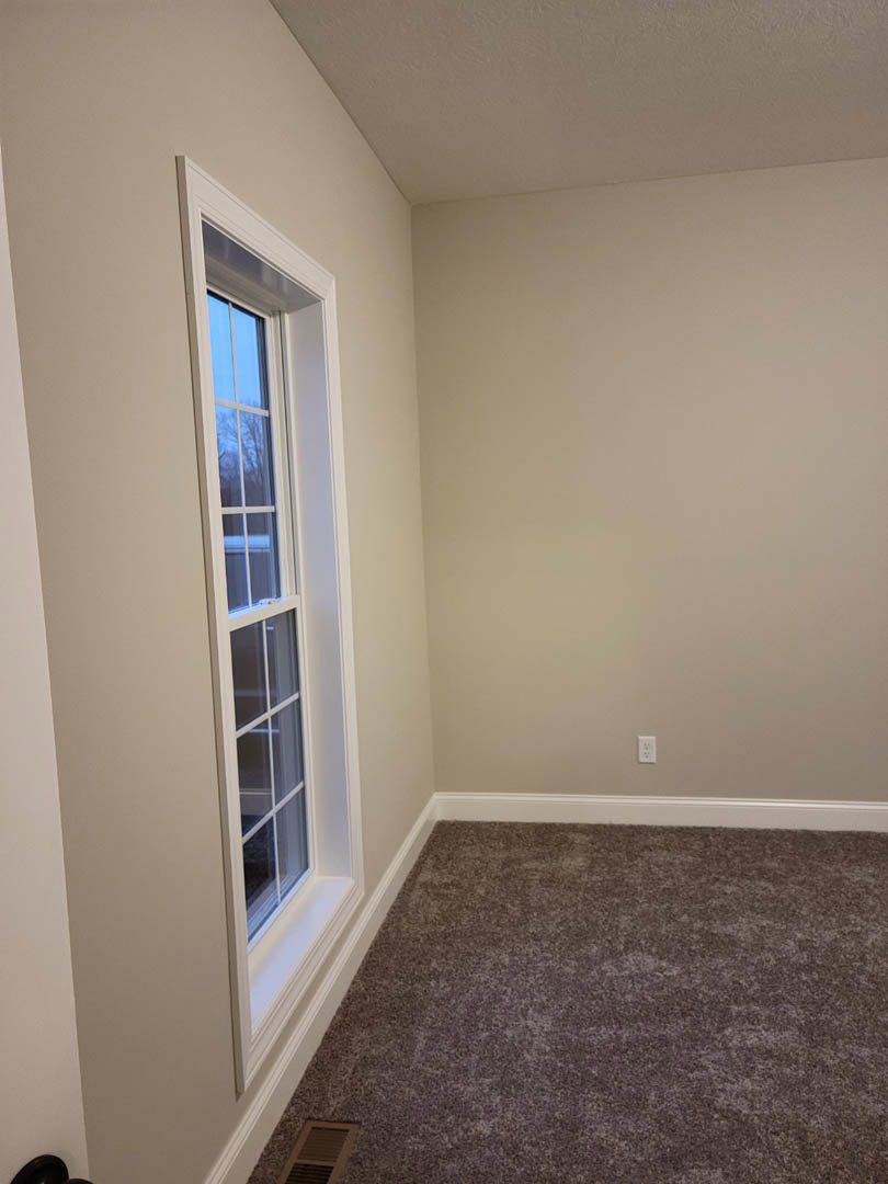 Carpeted floor, white walls and baseboards, window with white trim, ceiling vent, recessed ceiling light