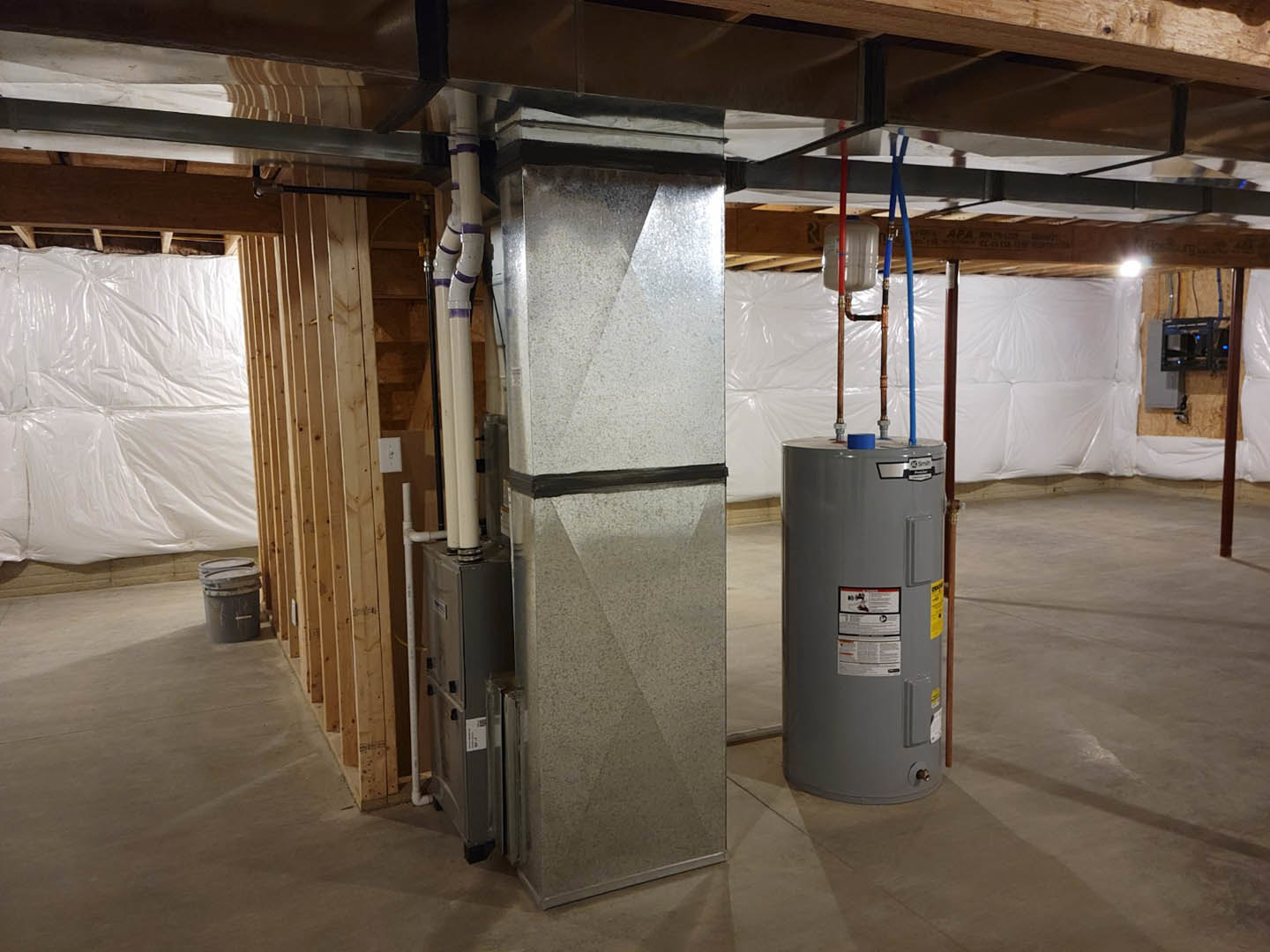 Large grey cylindrical tank positioned on a concrete basement floor, surrounded by exposed beams, white walls, and nearby shelving.