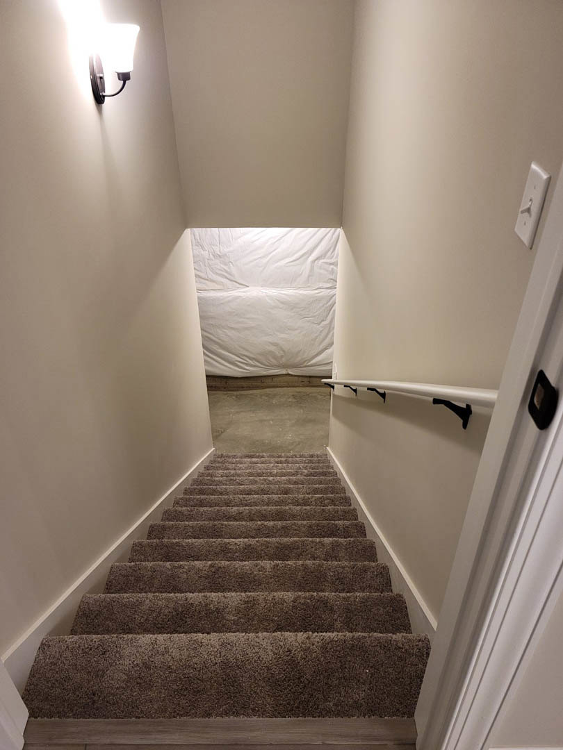 Wooden staircase with white plaster walls, recessed wall light, and minimalist handrail in modern interior.
