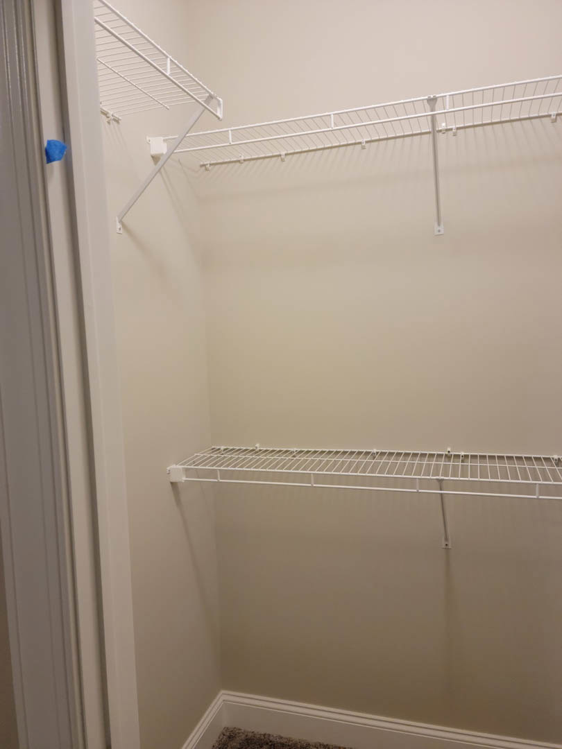 White closet with built-in shelves, metal bars, and white molding on the wall, adjacent to a door.
