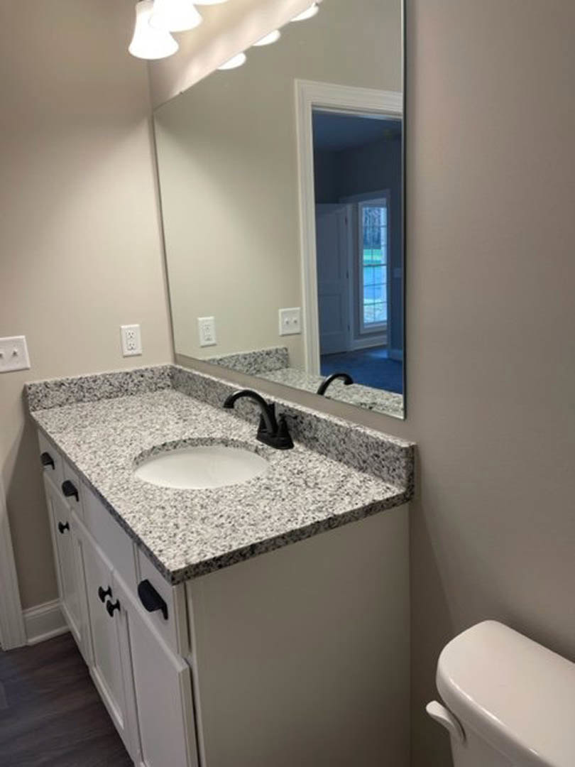 Modern bathroom with white quartz countertop, black trim, rectangular sink, chrome faucet, large framed mirror, and partial view of toilet tank against tiled wall