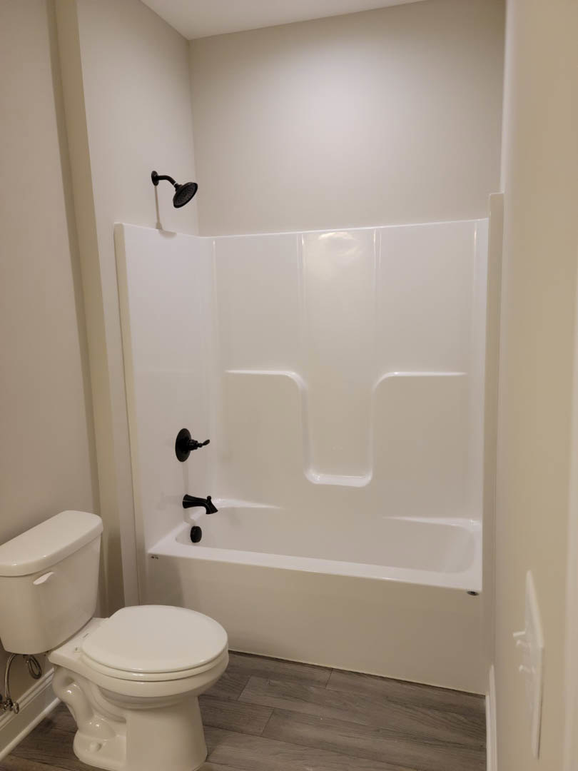 White freestanding bathtub with black faucet beside white toilet, light tile walls, and minimalist bathroom fixtures
