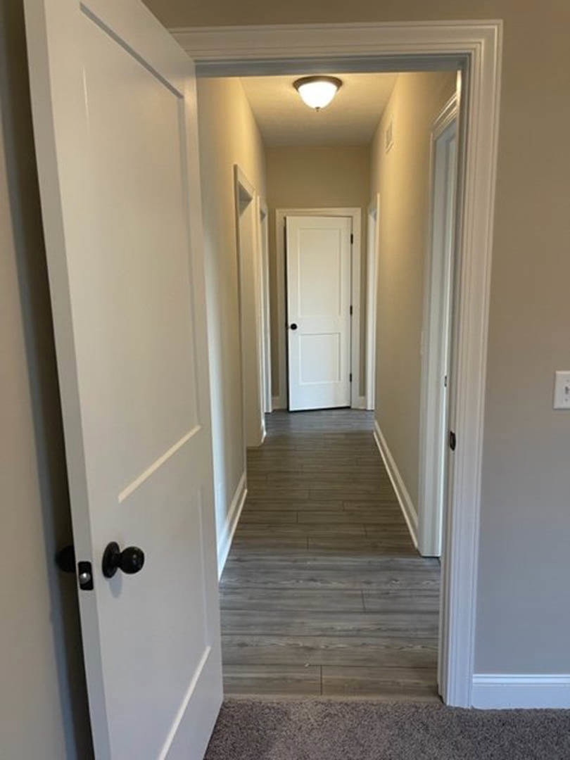 Hallway with white paneled doors, black door knobs, wood flooring, ceiling light fixture, and white walls with crown molding