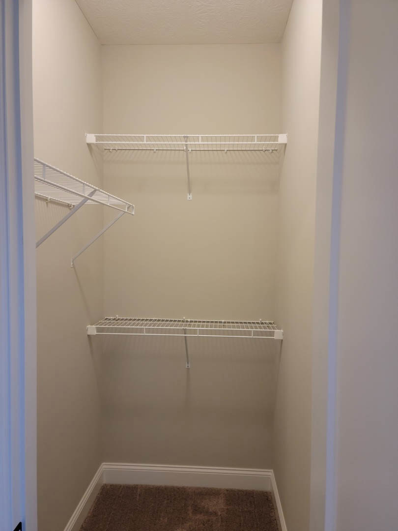 Walk-in closet with white shelving, metal hanging rod, and smooth plaster walls