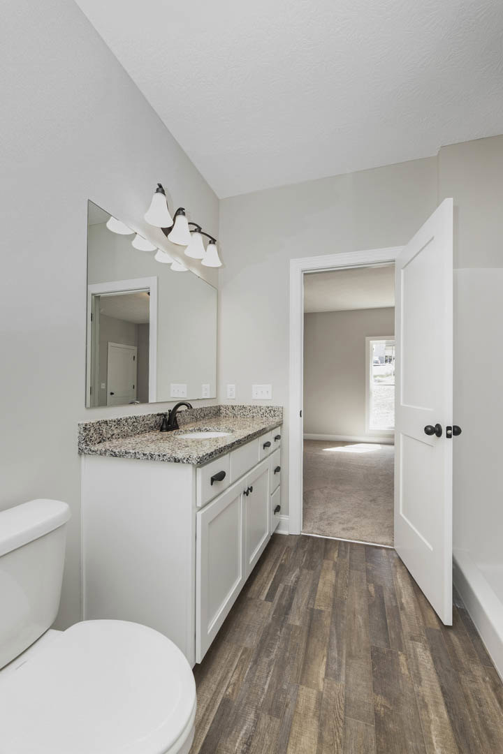 Marble countertop with undermount sink, white cabinetry, wood flooring, modern toilet, ceiling lights, sunlight streaming through window, interior door visible