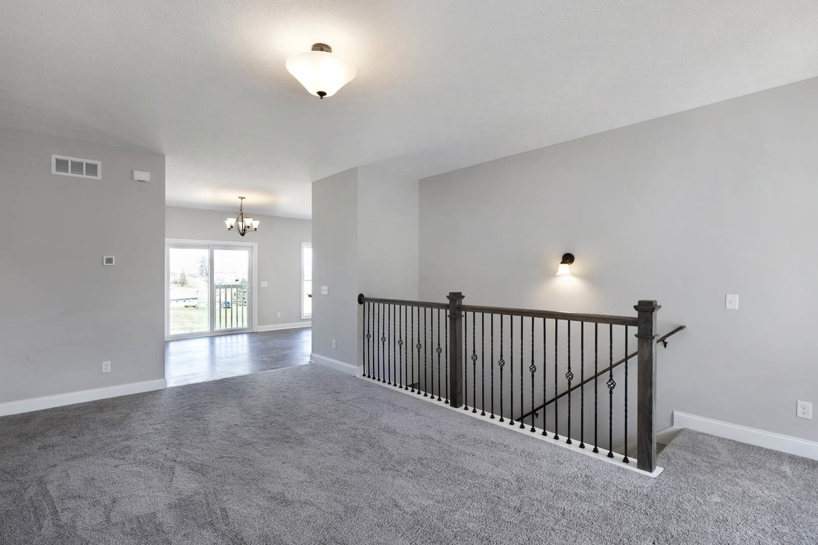 Wood staircase with metal handrail, white plaster walls, modern chandelier, large window overlooking fenced yard with grass