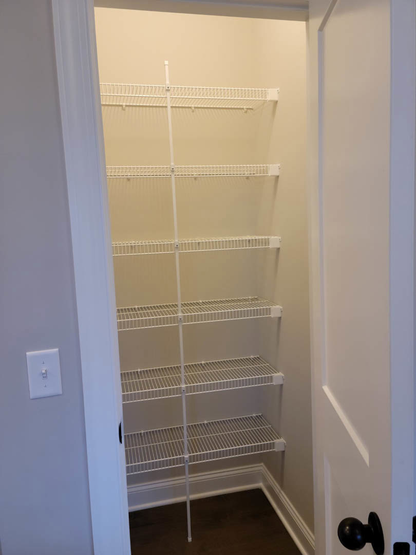 White closet with built-in shelves, white walls, black door knob, white metal air vent, and a light switch.