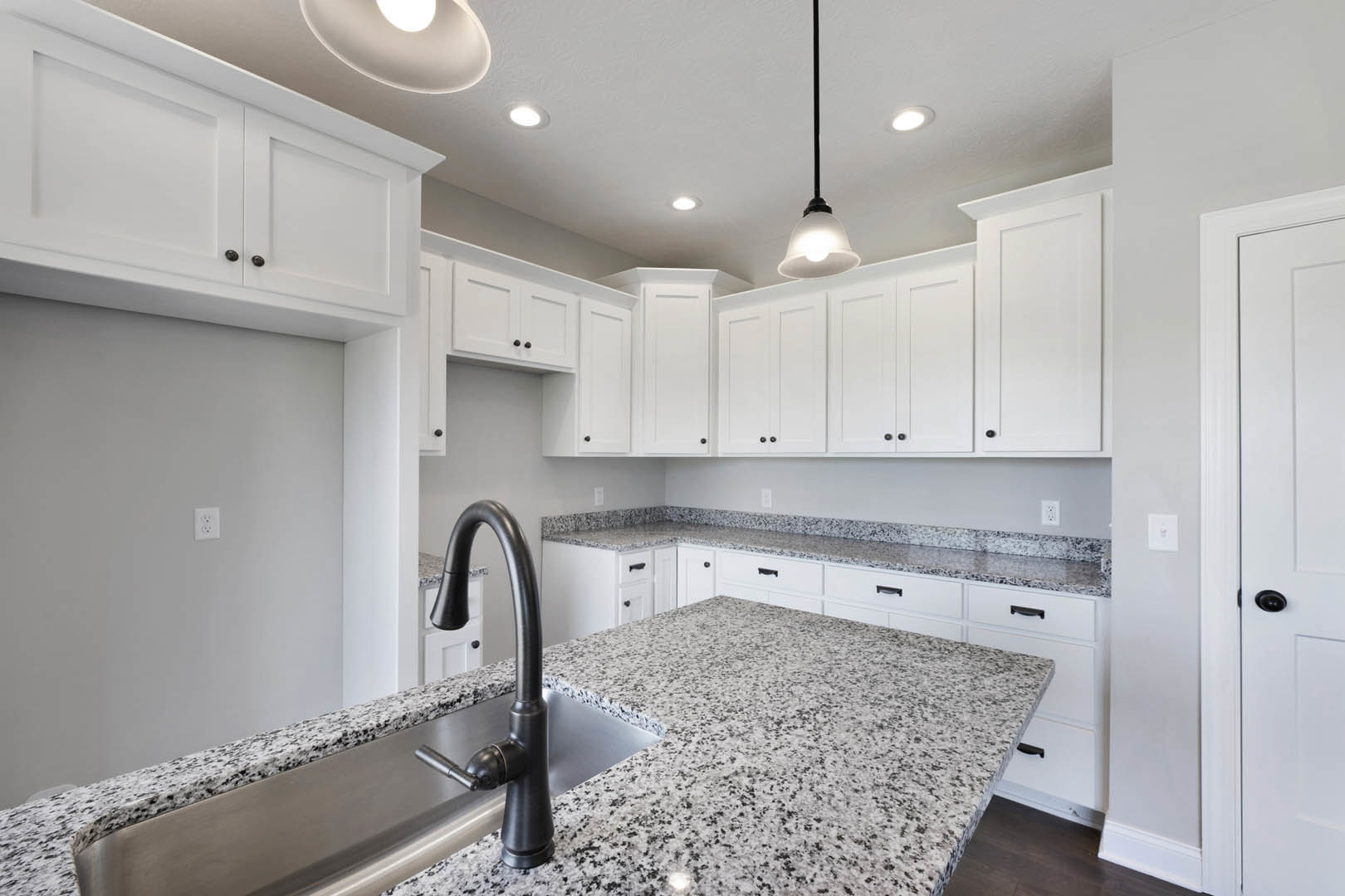 Kitchen with white shaker cabinets, speckled granite countertops, stainless steel faucet, undermount sink, tile backsplash, and brushed metal door knob