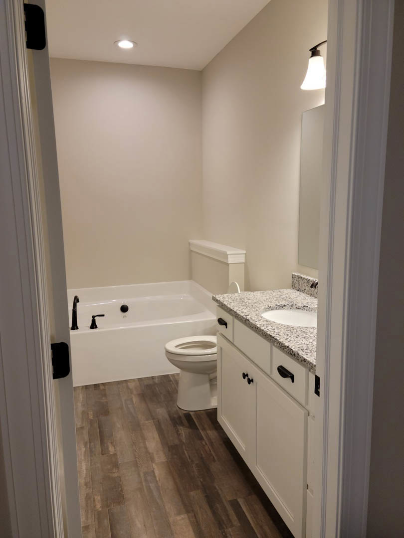 White porcelain sink and toilet beside a wood floor, white cabinet, and tiled wall in a modern bathroom.