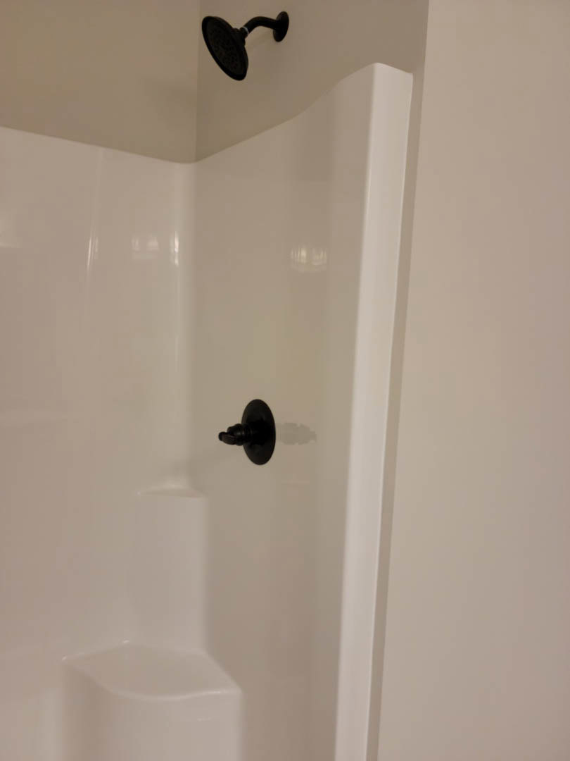 Freestanding white bathtub with matte black faucet and shower head against a white tiled wall in a modern bathroom