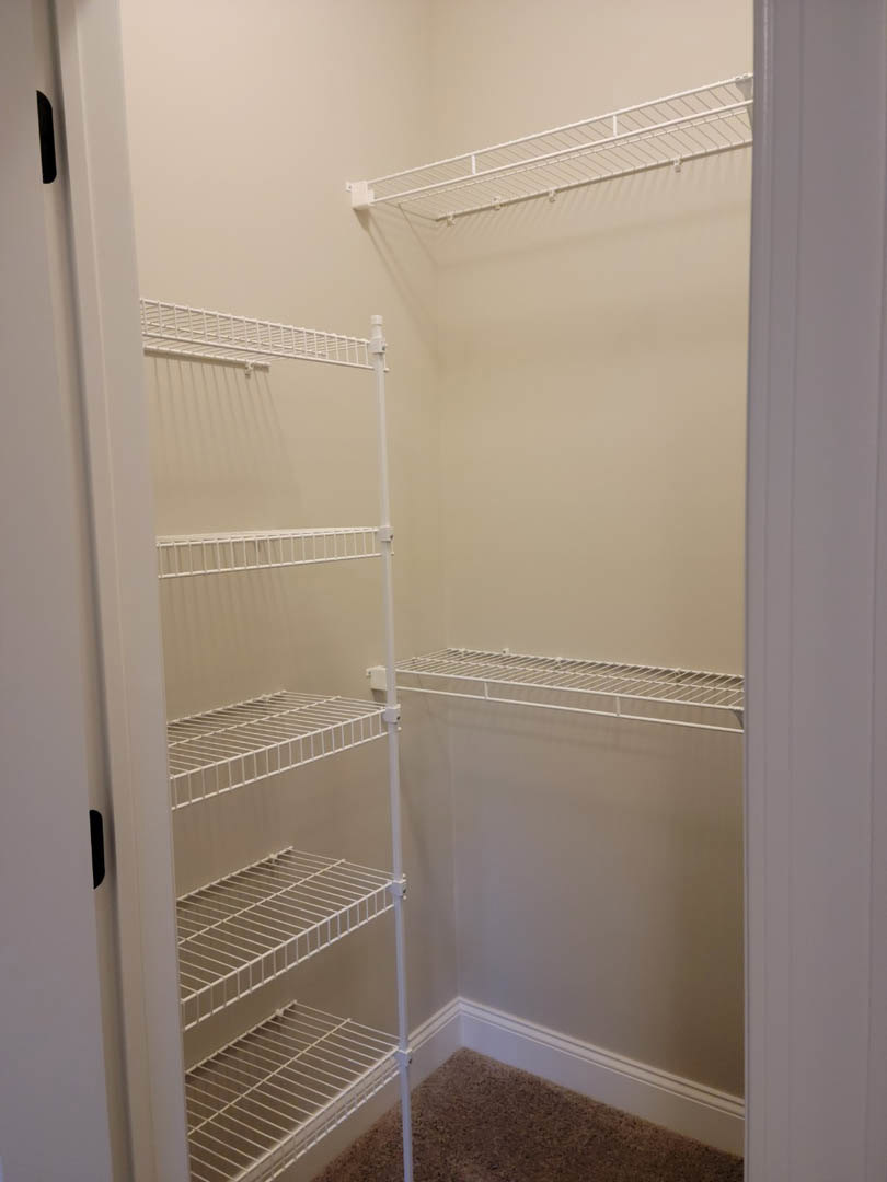 Walk-in closet with white wire shelves mounted on plaster walls, beige carpet flooring, and a white door partially visible