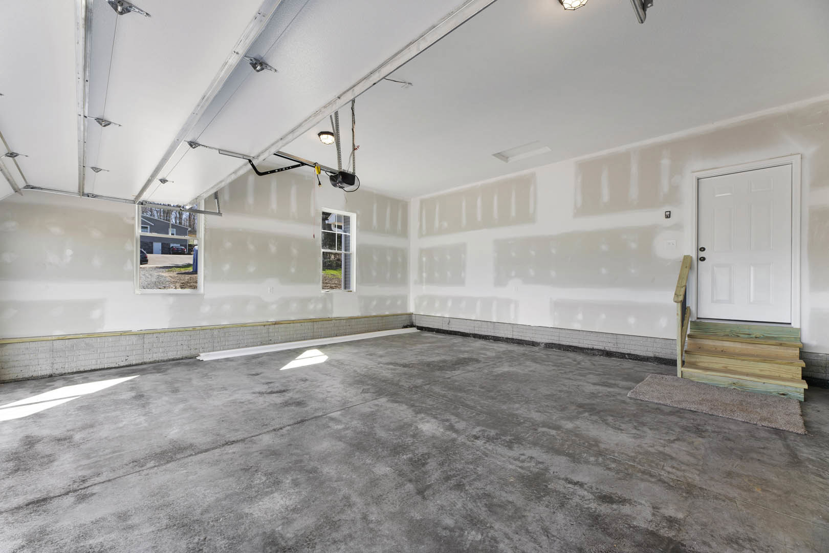 Concrete floor with white plaster walls, wood plank accent wall, white door with black handle, window with white frame, metal ladder leaning against wall