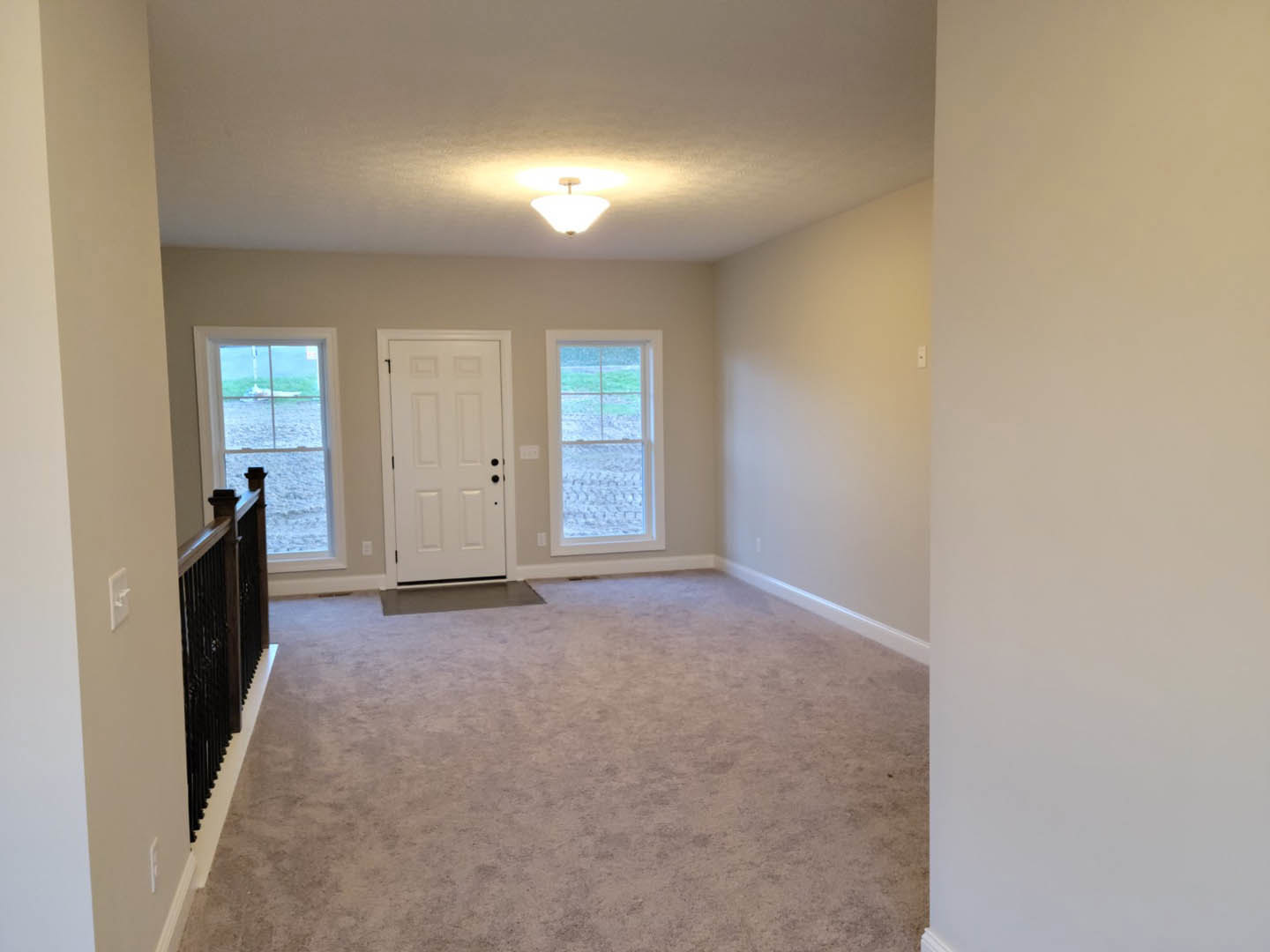 Hallway with light carpet flooring, white door featuring black knobs, white railing, ceiling-mounted light fixture, and window overlooking water with a boat visible.