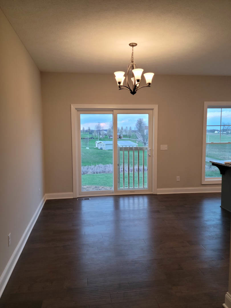 Hardwood floored room with sliding glass door overlooking green field and fence, chandelier hanging from ceiling, plaster walls, large window framing outdoor view