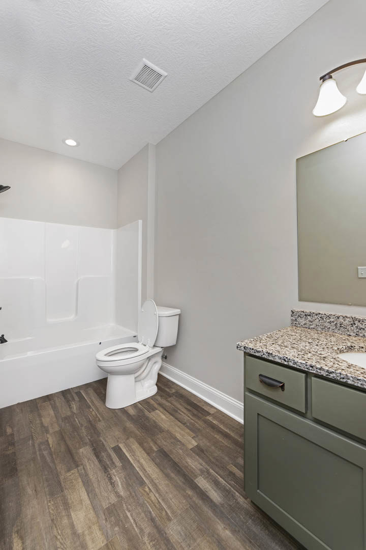 Modern bathroom with white toilet and rectangular sink, wood floor, tile walls, ceiling vent, and built-in cabinetry