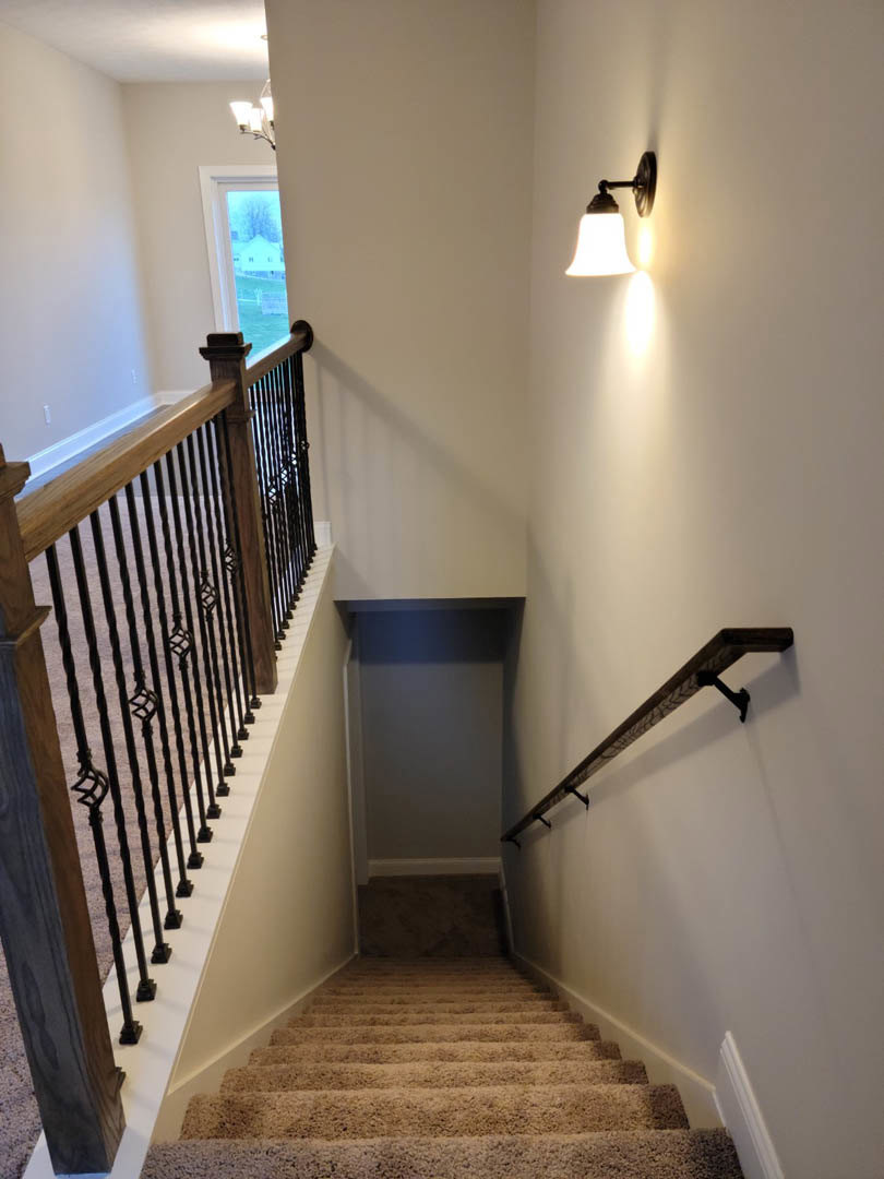 Wooden staircase with metal handrail, white plaster wall, and modern wall-mounted light fixture