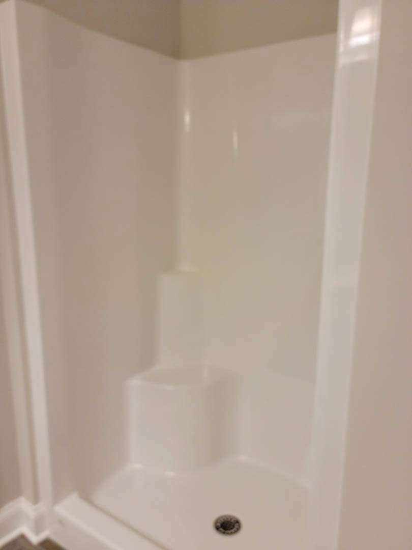 White tile shower stall with built-in steps and plaster walls, adjacent to a sink drain.
