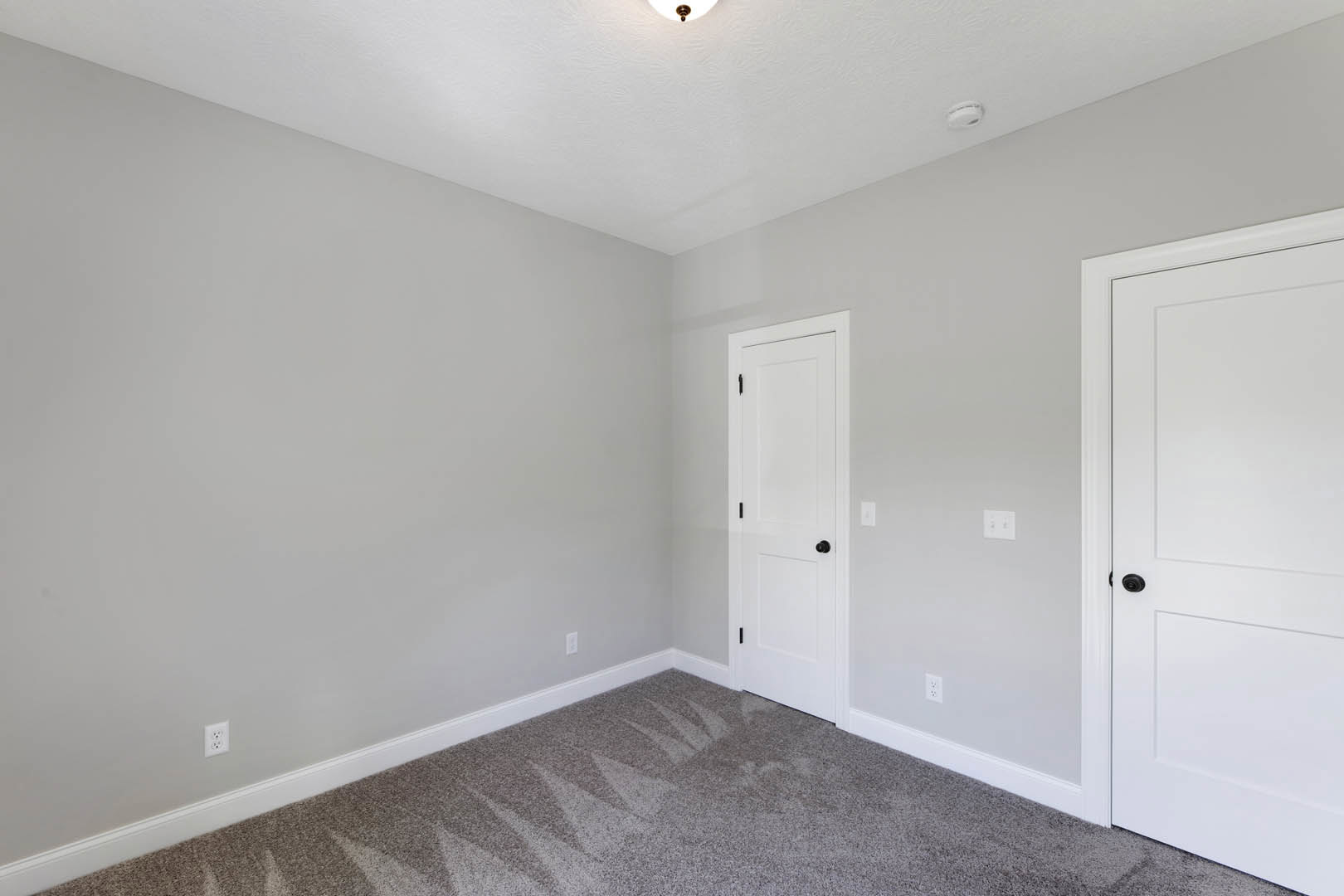 Carpeted room with white walls, white ceiling light, and white doors featuring black knobs; visible scratches on the carpet.