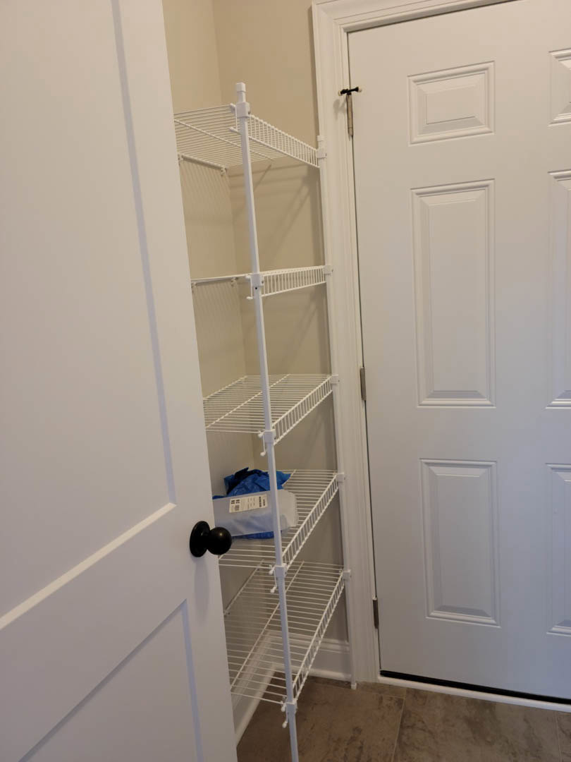 White shelf mounted in a closet with a white door and silver handle, white plastic container with label, black balloon resting on white surface, white door frame, close-up of