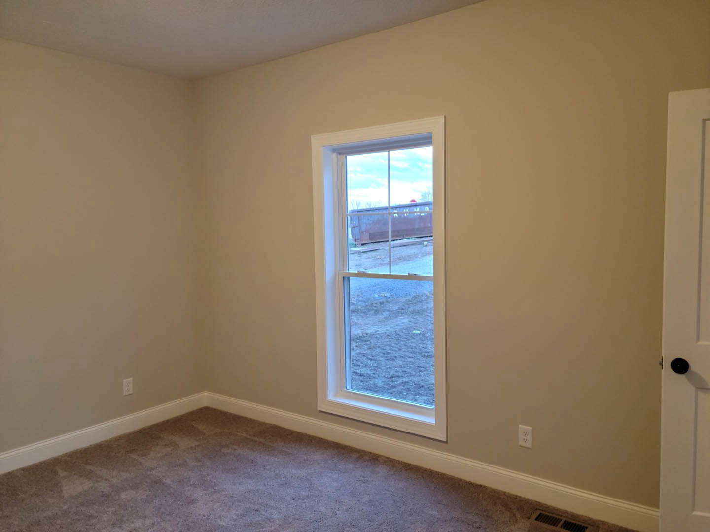 White-walled room featuring a large window with black trim, snowy field visible outside, light carpet flooring, and metal bar across the window.