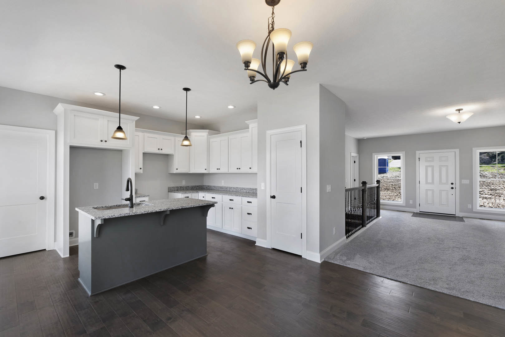 Open kitchen and living room featuring a central chandelier, white cabinetry, stone countertop with built-in sink, stainless steel appliances, hardwood flooring, white doors with