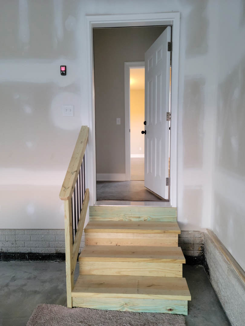 Wooden staircase with carpeted steps, white door open to hallway, close-up of wooden handrail and balusters, plaster walls, hardwood flooring