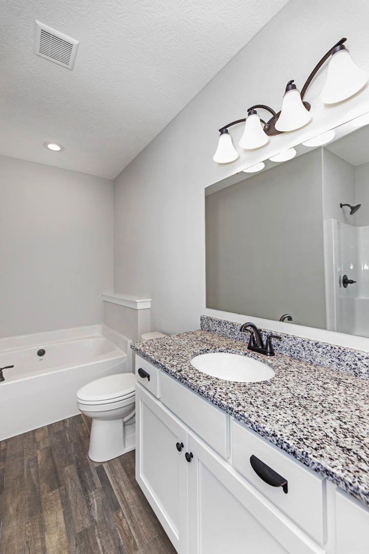 Marble countertop with black faucet, freestanding bathtub, white toilet, four-light ceiling fixture, vent, and stone tile surfaces in a modern bathroom.