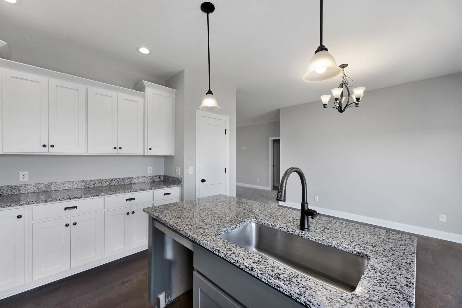 Granite countertops, white shaker cabinets with black knobs, black curved faucet, stainless steel sink, tile backsplash