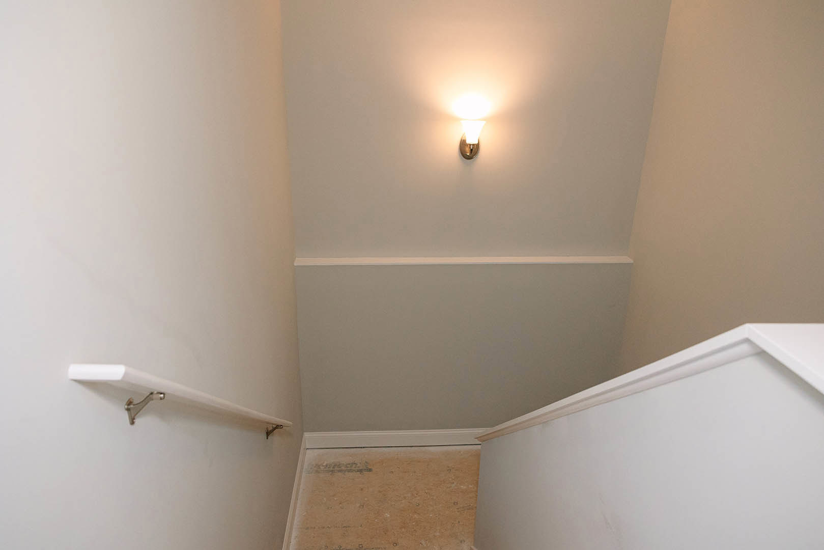 Wall-mounted sconce with a metal base and frosted glass shade on a white plaster bathroom wall, brown accent surface visible nearby