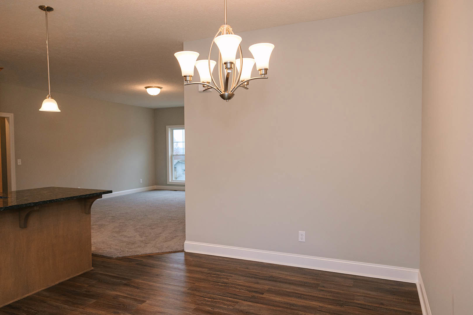 Modern chandelier with glass shades hanging above a marble kitchen island, white cabinetry, laminate flooring, and large window with white trim.
