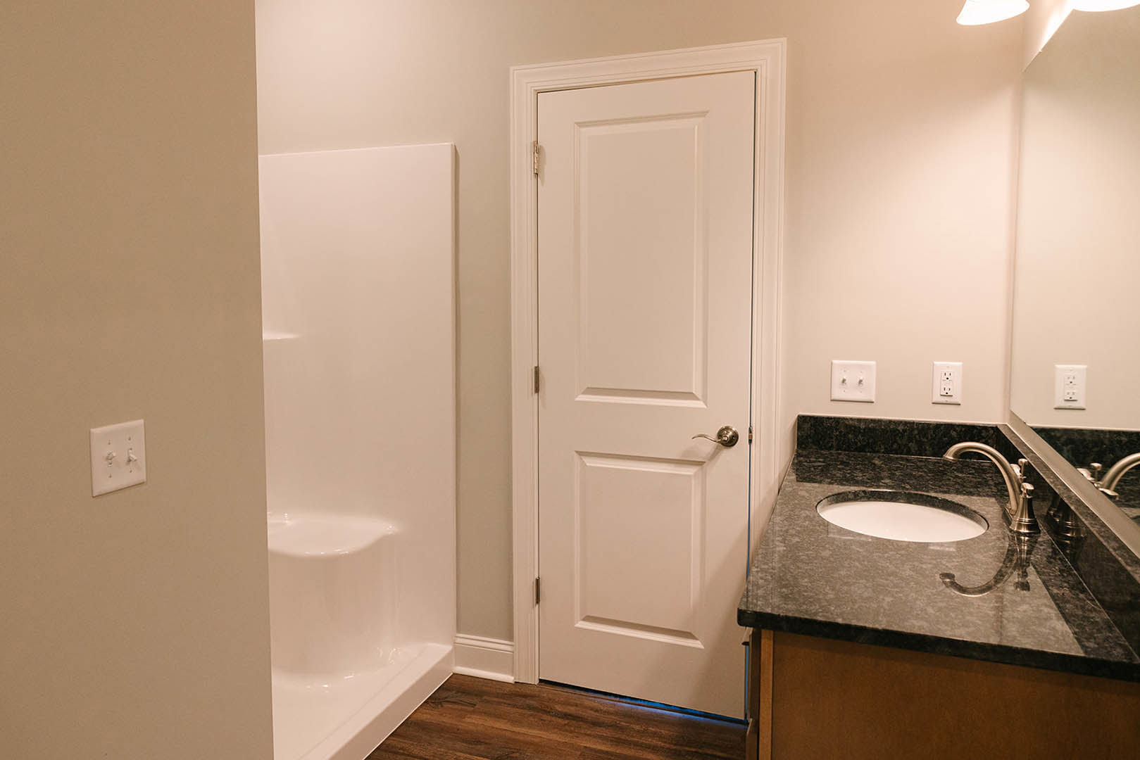 Modern bathroom featuring a white sink with black border, tiled walls, glass shower enclosure, white door with silver handle, and visible light switch and wall outlet.