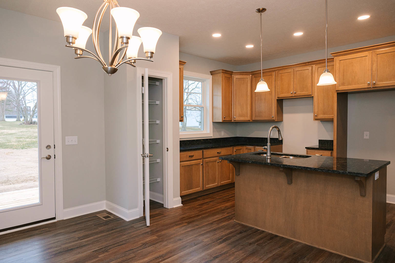 Spacious kitchen featuring a large central island with stone countertop, stainless steel refrigerator, modern cabinetry, built-in sink, glass door, chandelier, and window