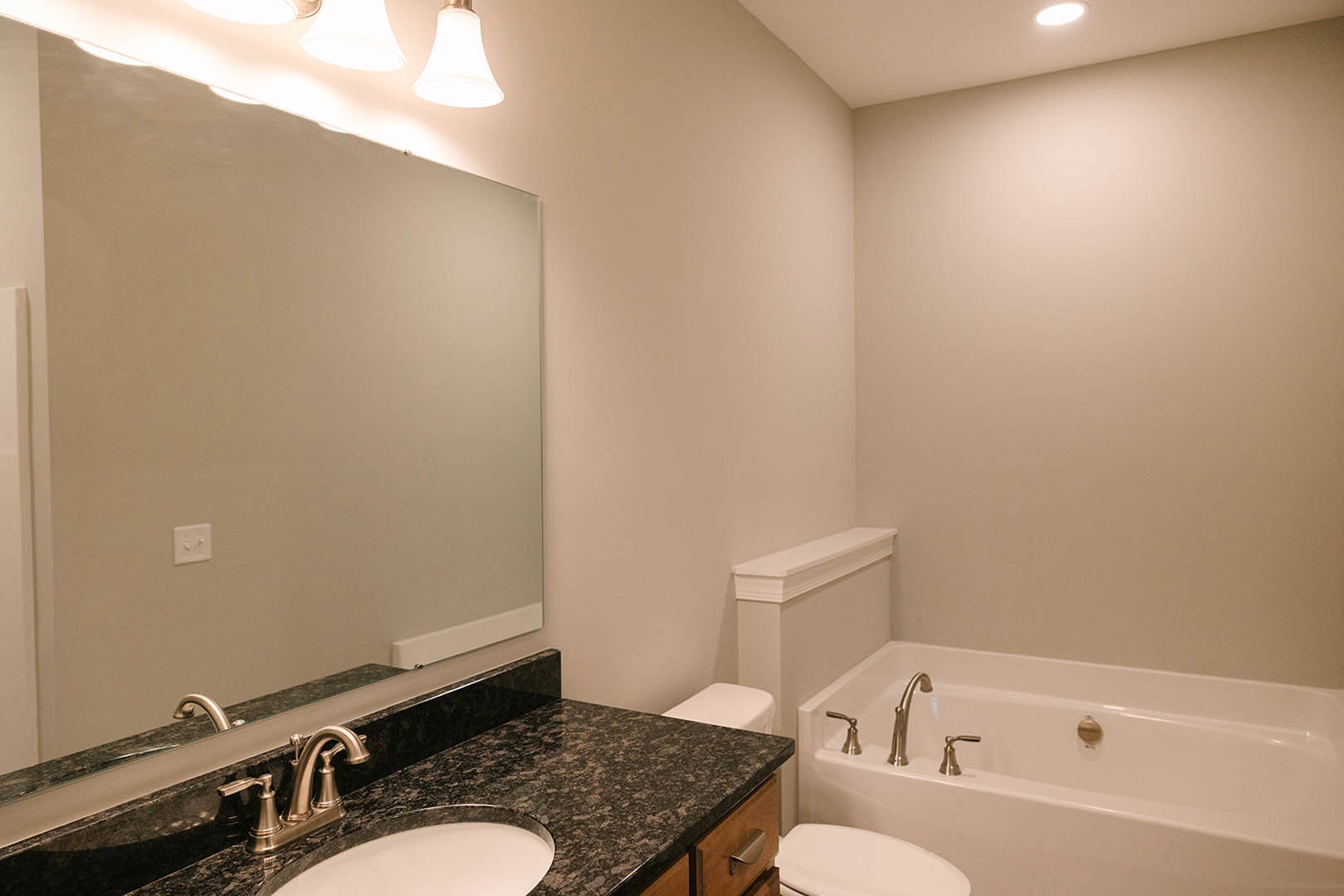Modern bathroom with white tile walls, built-in bathtub with chrome faucet, white porcelain sink, and toilet; two-knob light switch visible on wall