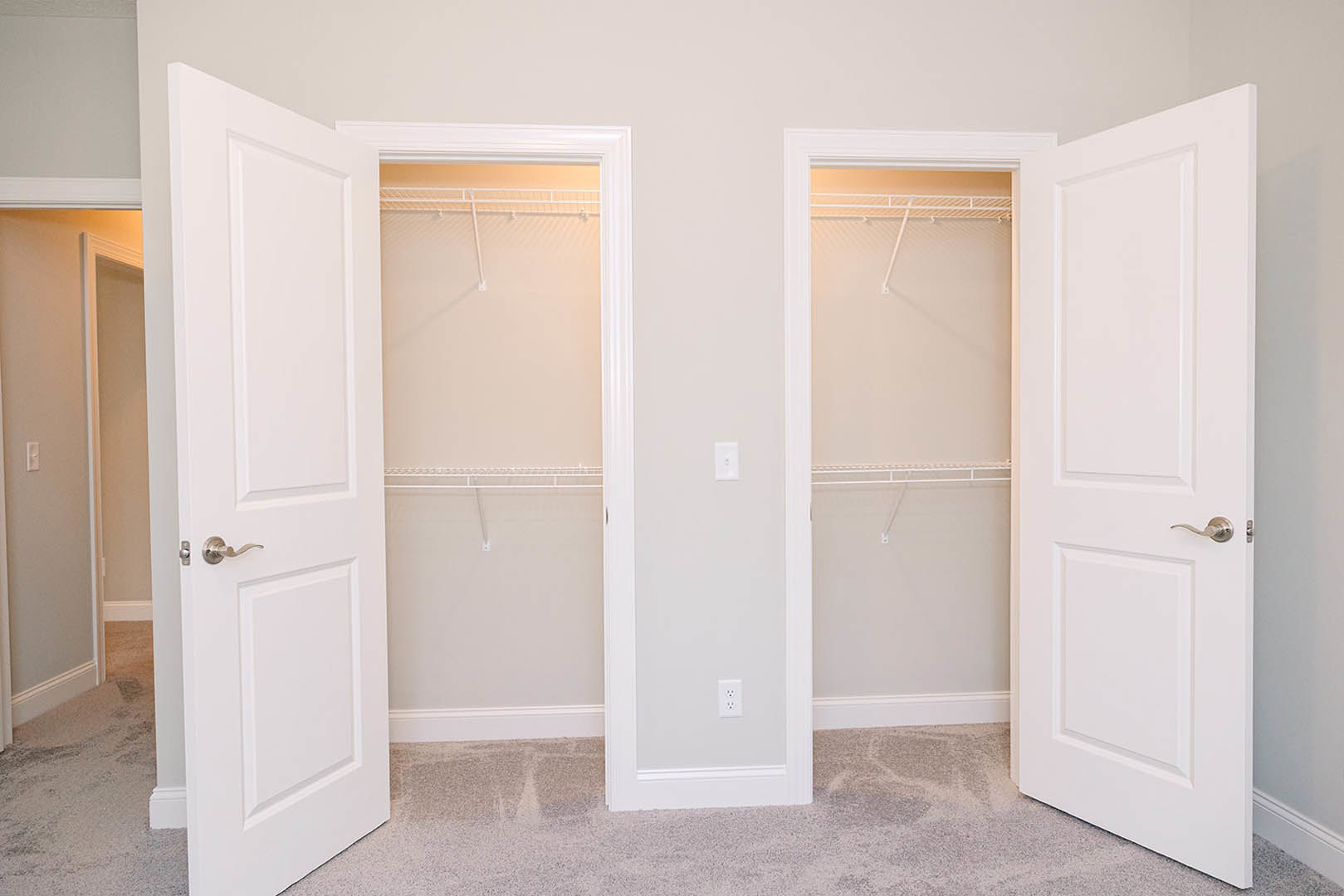 White closet with built-in shelves, double doors, white walls, light switch, and wood flooring