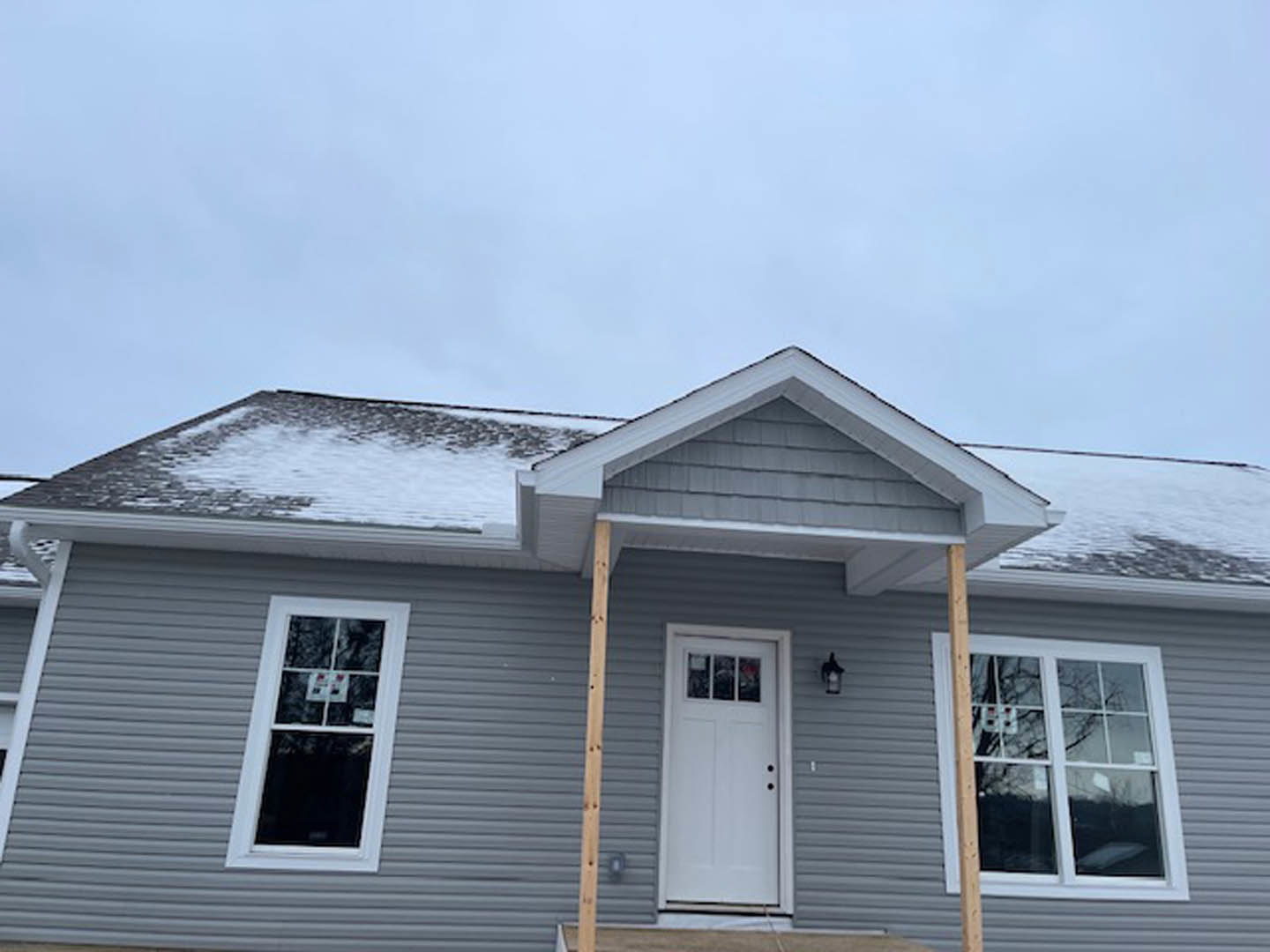 Two-story home with snow-covered roof, white siding, front porch supported by wooden posts, white framed windows, and a white entry door with glass panel