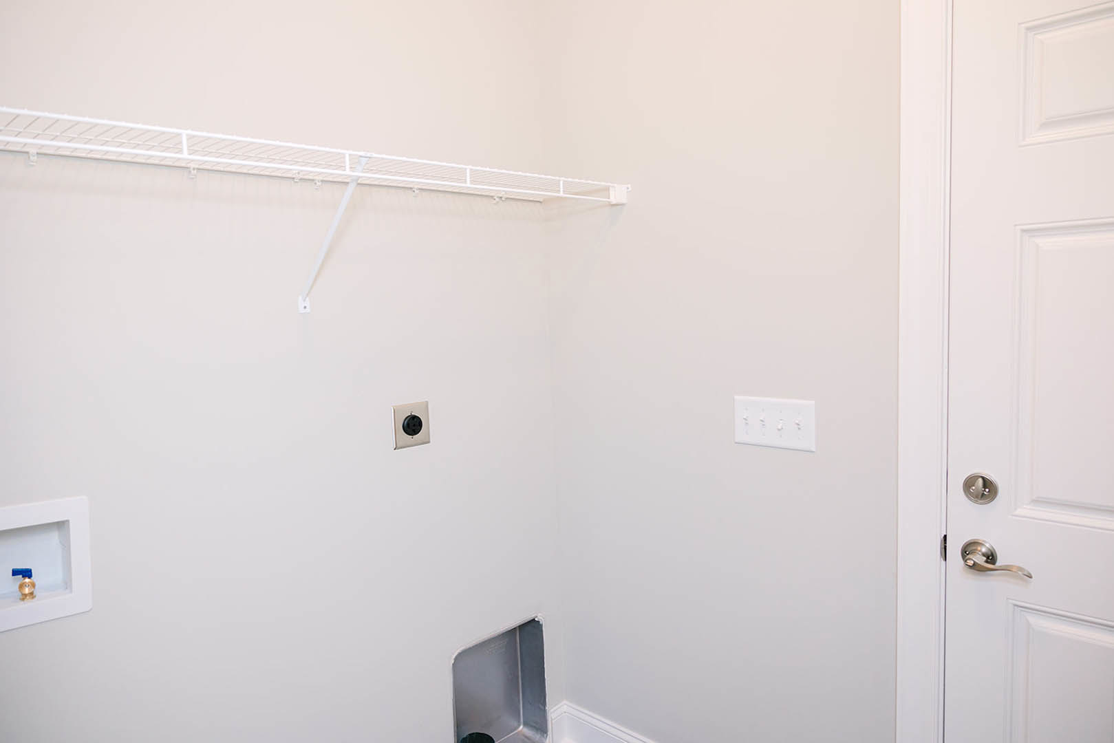 White built-in shelf against a plaster wall with visible electrical outlet and metal valve, located in a residential interior.